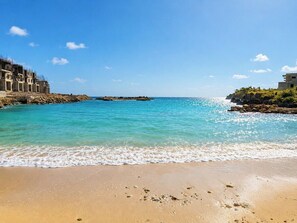 Une plage avec une eau turquoise et limpide, un rivage sablonneux et des bâtiments situés sur la gauche.