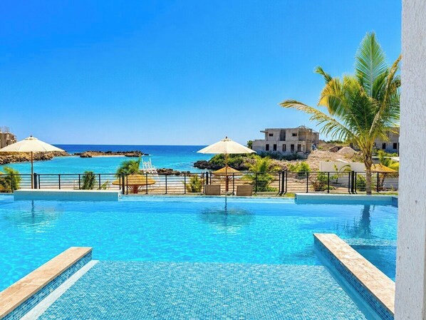 A clear blue pool with a view of the sea and a building in the background.