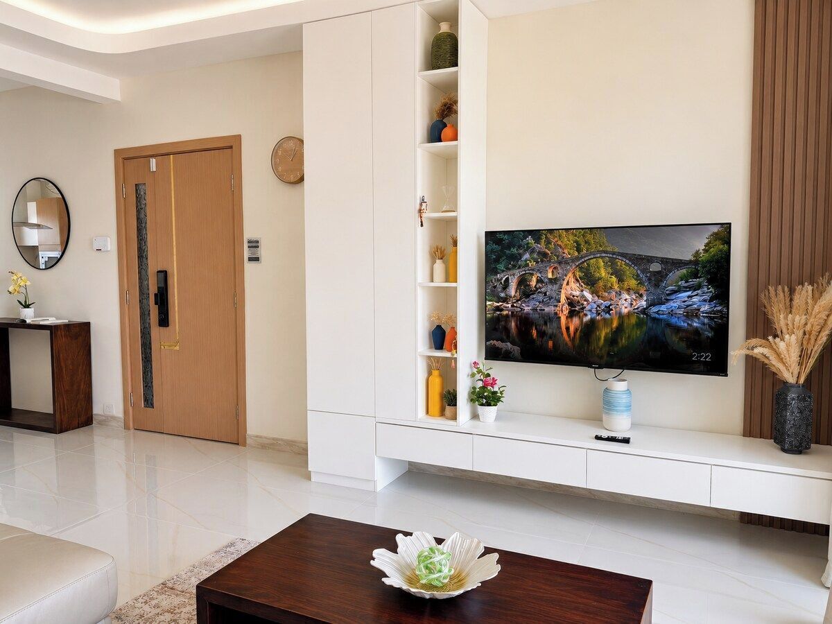 Una sala moderna con un televisor de pantalla plana montado en un mueble blanco, una puerta de madera y una mesita con un florero.