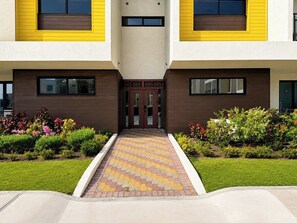 A modern building with a symmetrical facade, a central entrance with double doors, and a paved pathway leading to the entrance.