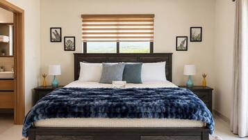 Un dormitorio con cama de madera oscura, ropa de cama blanca, una manta azul suave y una ventana con persianas.