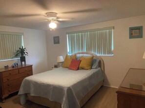 A bedroom with a bed, a dresser, a nightstand, a lamp, a ceiling fan, and a window with blinds. - Charming 2-bedroom house with pool in Englewood (Englewood)
