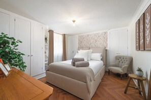 A bedroom with a bed, a chair, a wooden table, and a potted plant.