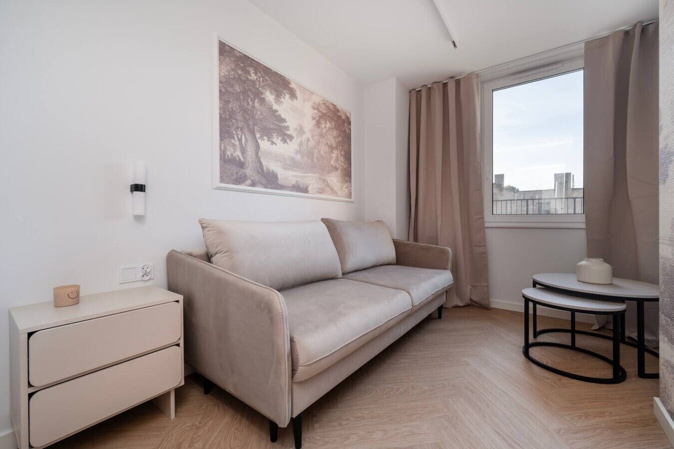 Ett stilrent, minimalistiskt rum med en soffa, ett litet sidobord, en vägglampa och ett fönster med gardiner.