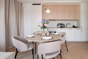 A modern dining area with a round table, four chairs, a vase of flowers, and a kitchen in the background. - Łódź City Center Apt — Parking & Terrace (Łódź)