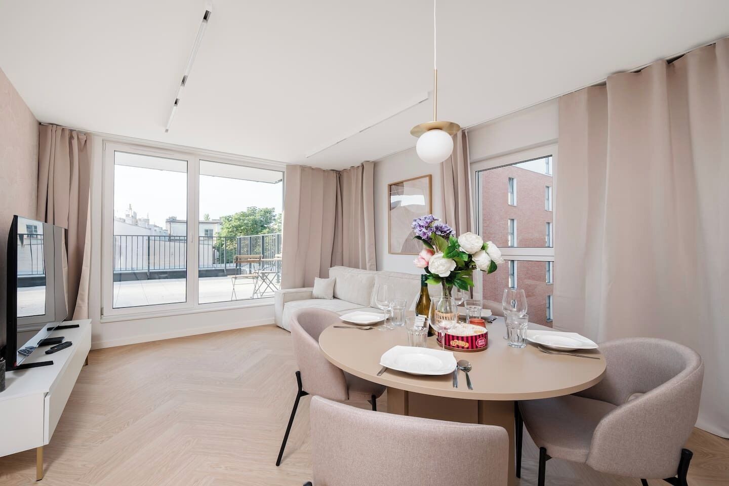A modern dining area with a round table set for two, a sofa, and a television on a stand.
