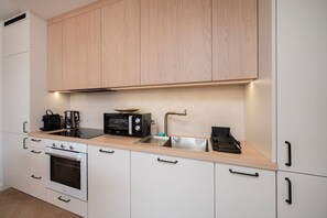 A modern kitchen with white cabinetry, a built-in oven, a microwave, a kettle, and a sink. - Łódź City Center Apt — Parking & Terrace (Łódź)