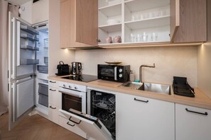 Et kompakt køkken med hvide skabe, en indbygget ovn, en mikrobølgeovn og en vask med en moderne hane.