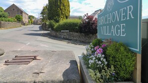 Señal de calle que indica el pueblo de Birchover, con un muro de piedra y plantas en flor.