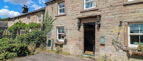 A stone cottage with a tiled entrance, a green door, and a small garden area.