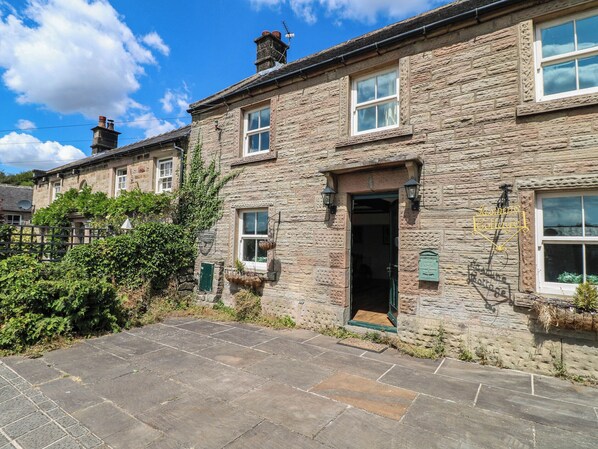 A stone cottage with a tiled entrance, a green door, and a small garden area.