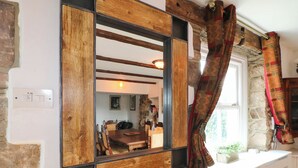 Una habitación con un espejo grande que refleja un comedor, una pared de piedra y una ventana con cortinas.