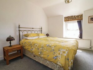 A bedroom with a bed, a nightstand, a lamp, a window with curtains, and a radiator.