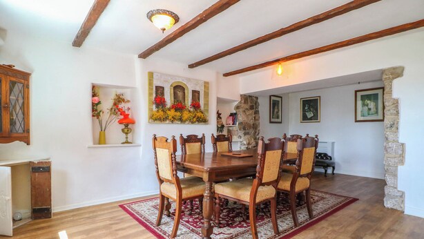 Un comedor con una mesa y sillas de madera, un tapete de diseño rojo y blanco, y una pared de piedra.