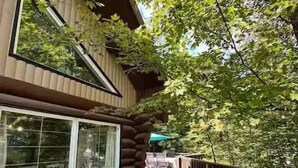 Une terrasse en bois avec un espace repas, une grande fenêtre et une vue sur les arbres.