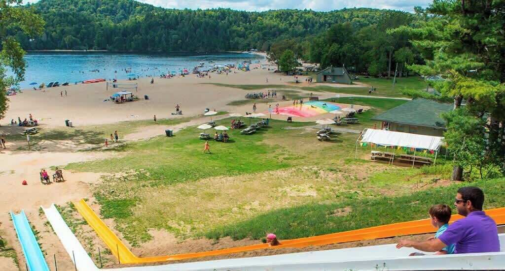 A beach with a water slide, a sandy area, and a grassy field with tents.