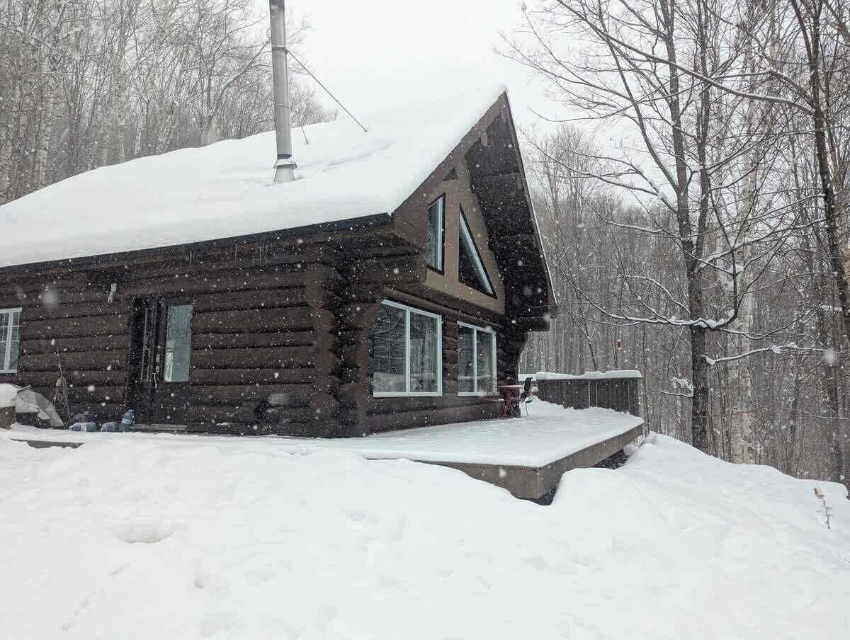 A log cabin with a snow-covered roof and a chimney, surrounded by a snowy landscape.