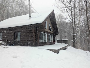 Eine Blockhütte mit schneebedecktem Dach und Schornstein, eingebettet in eine verschneite Winterlandschaft.