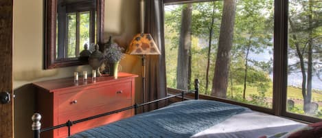 Un dormitorio con cama, cómoda, espejo, lámpara y vistas a árboles y agua.