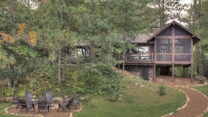 A cabin with a deck, surrounded by trees and a landscaped garden with outdoor seating.