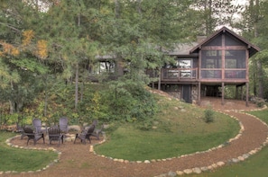 A cabin with a deck, surrounded by trees and a landscaped garden with outdoor seating.