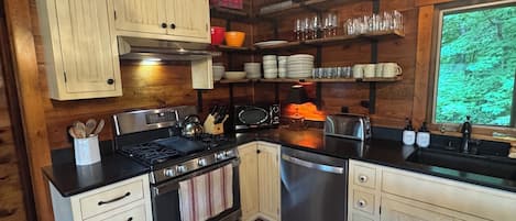 A kitchen with wooden cabinets, a stove, a dishwasher, and a window with a view of trees.