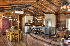 A rustic cabin interior with a dining area, kitchen, and a cozy seating area.
