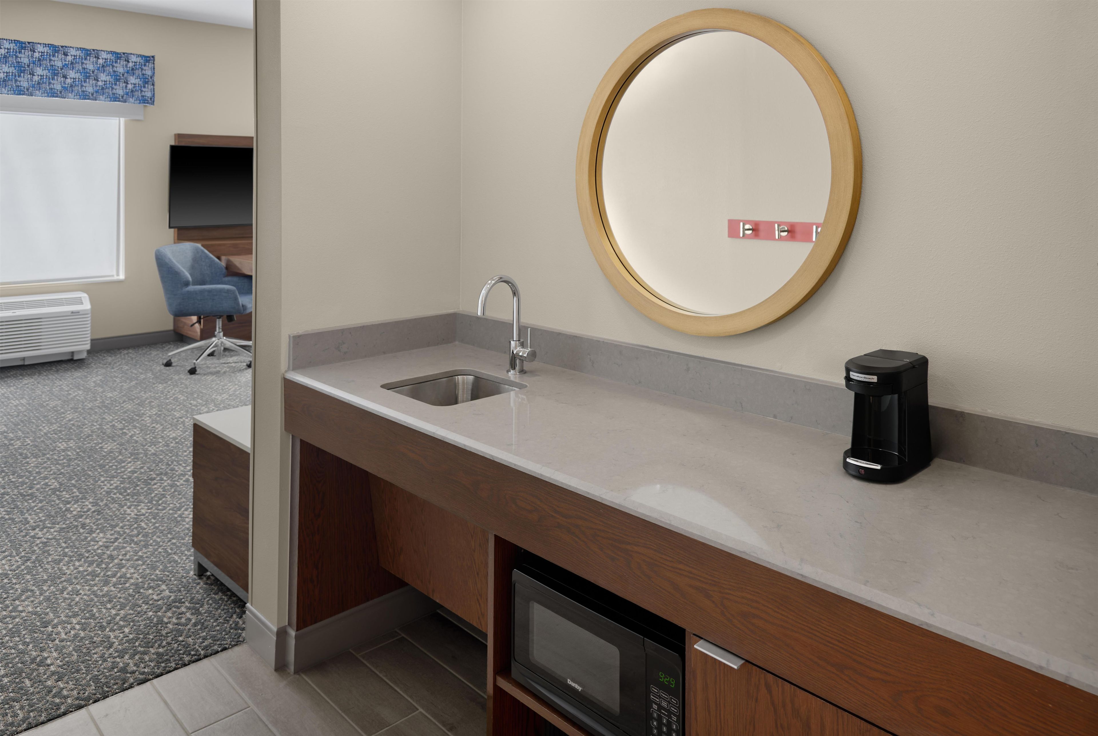 Un baño moderno con lavamanos, espejo, cafetera y microondas.