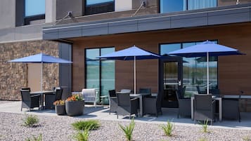 Un espace extérieur aménagé avec des tables et des chaises, des parasols bleus et un mur en pierre.