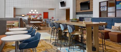 Un hall d’hôtel moderne avec un bar central, des espaces de détente et un comptoir pour le petit-déjeuner.