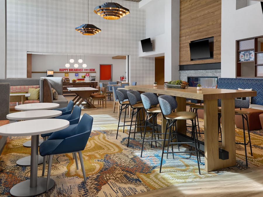 Un hall d’hôtel moderne avec un bar central, des espaces de détente et un comptoir pour le petit-déjeuner.