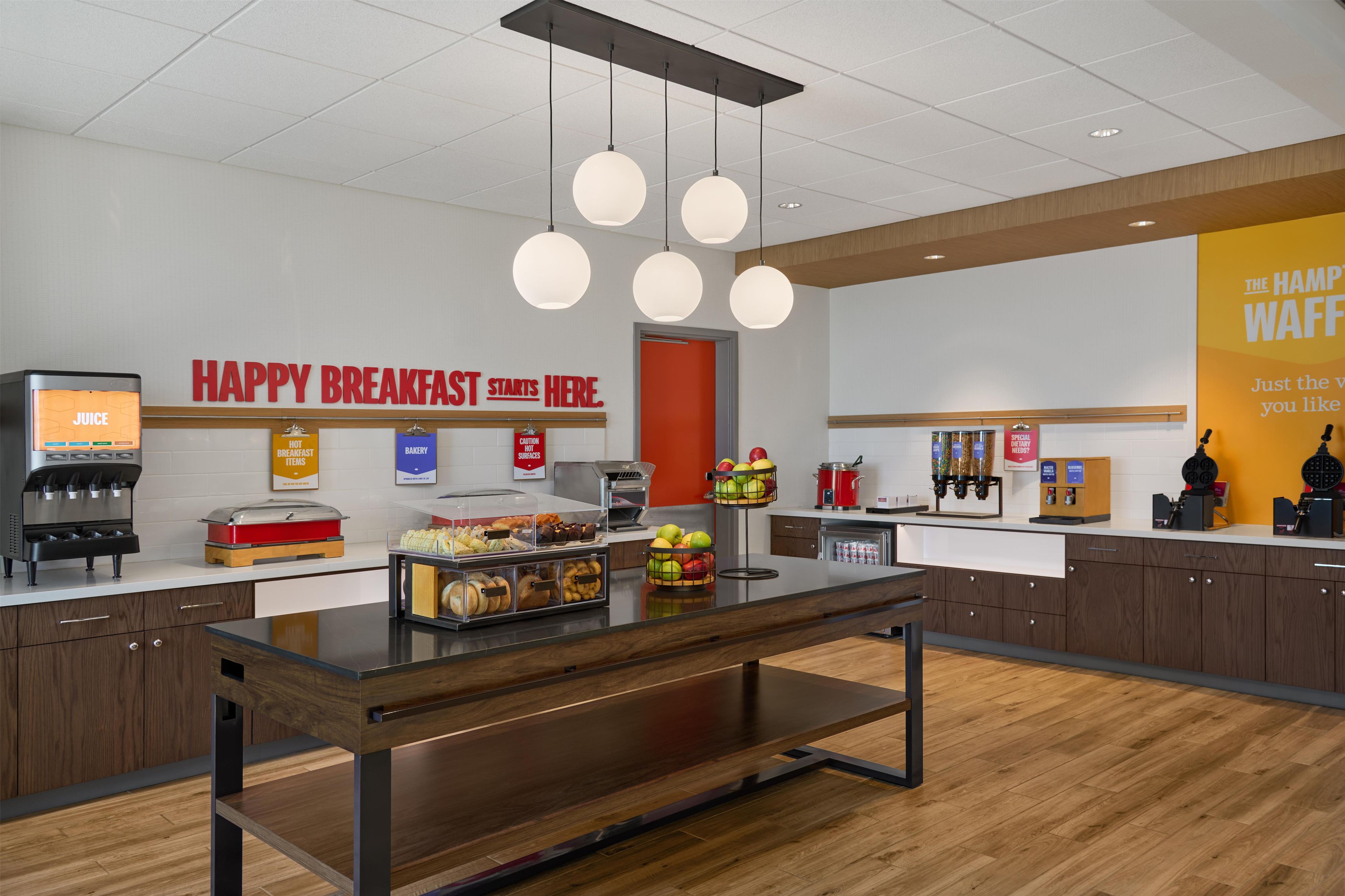 A modern breakfast area with a coffee machine, a juice dispenser, and a variety of food items on display.