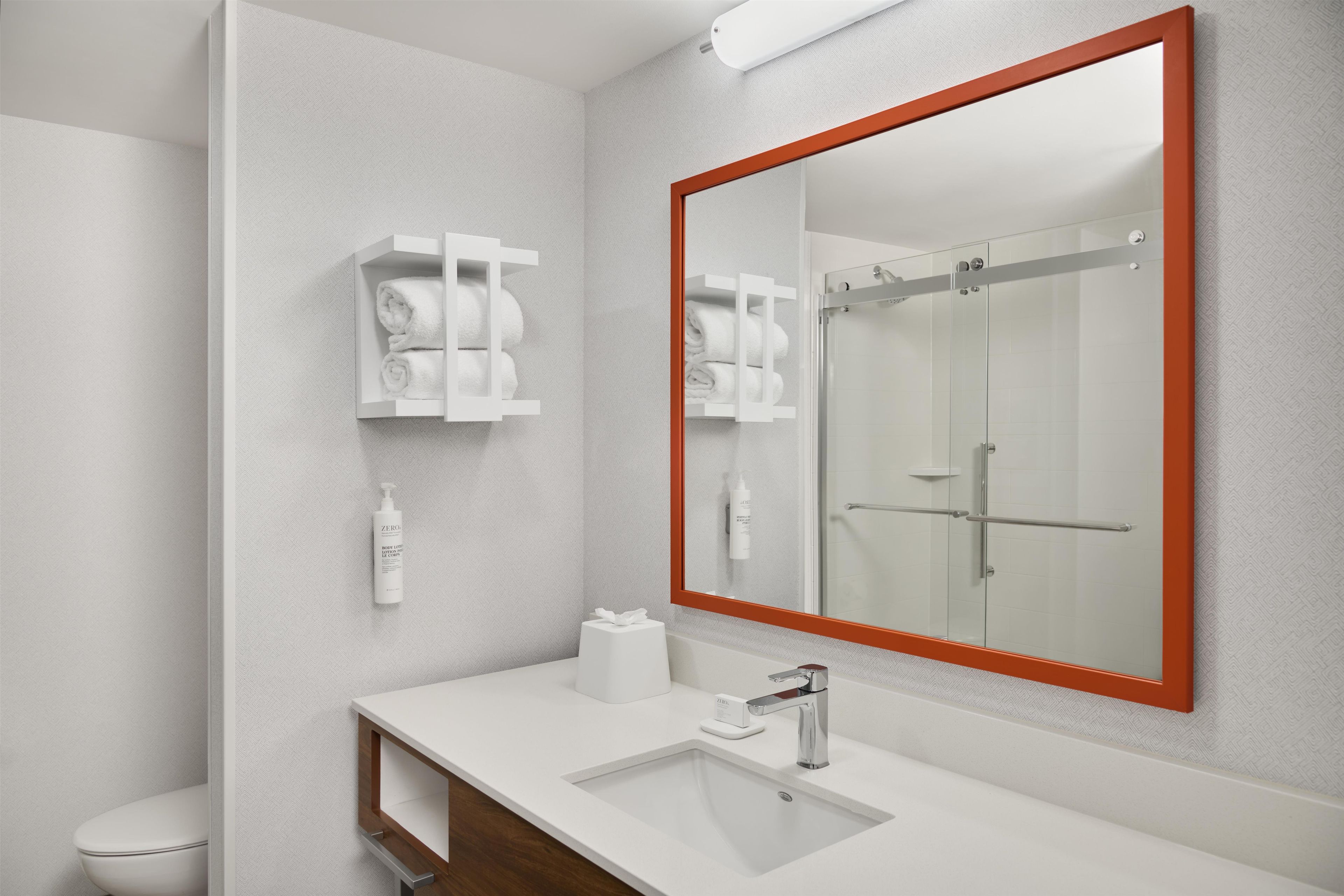 A modern bathroom with a large mirror, a white sink, and a glass shower enclosure.