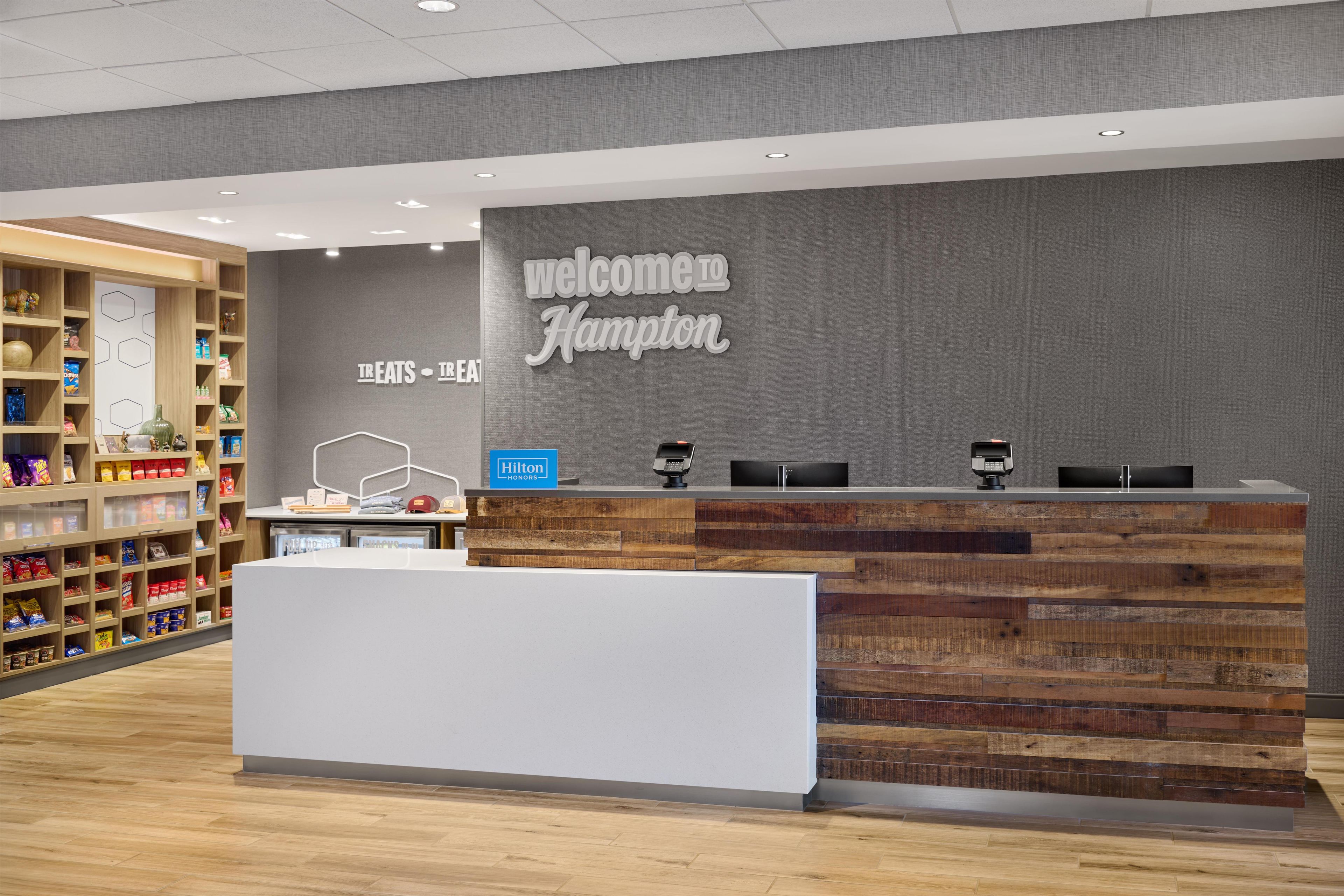 Un comptoir d’accueil avec une pancarte « Bienvenue à Hampton », un minibar et un présentoir de collations.