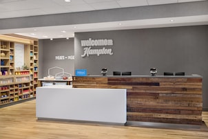 Bancada de recepção com placa 'Welcome to Hampton', minibar e exposição de lanches.