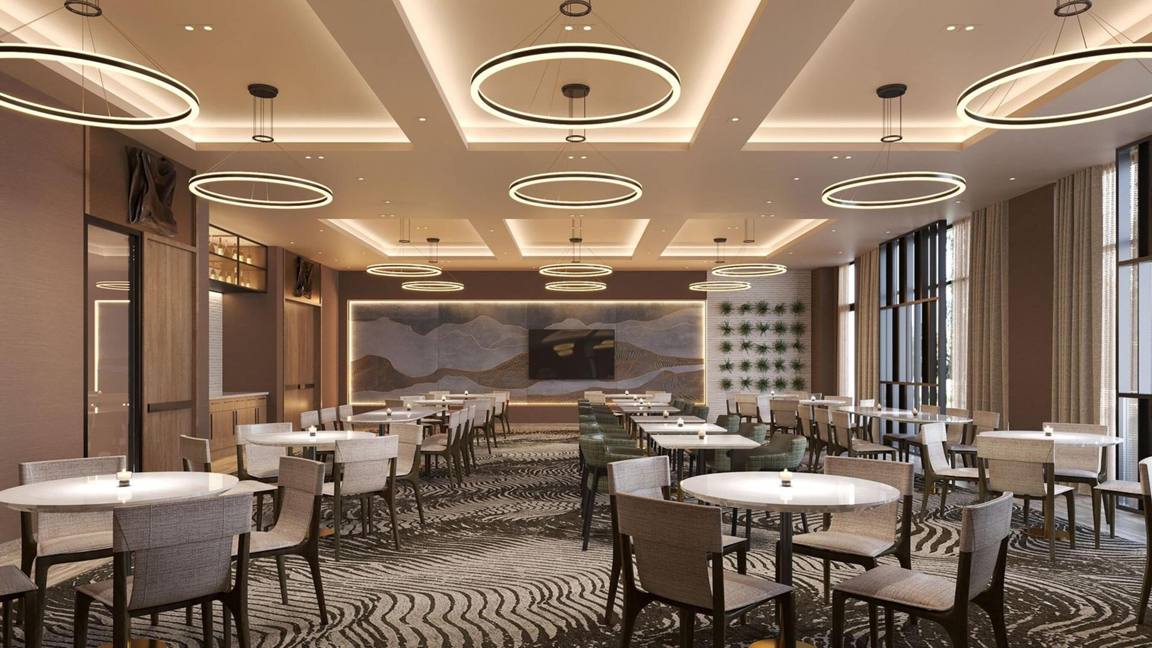 Un espace de restauration d’hôtel avec des tables rondes, des chaises et des luminaires modernes.
