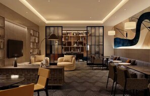 A modern living room with a sofa, armchairs, a coffee table, and a TV. There is a bookshelf and a dining area with a table and chairs. - Tempo By Hilton - Gallery Park (Mesa)