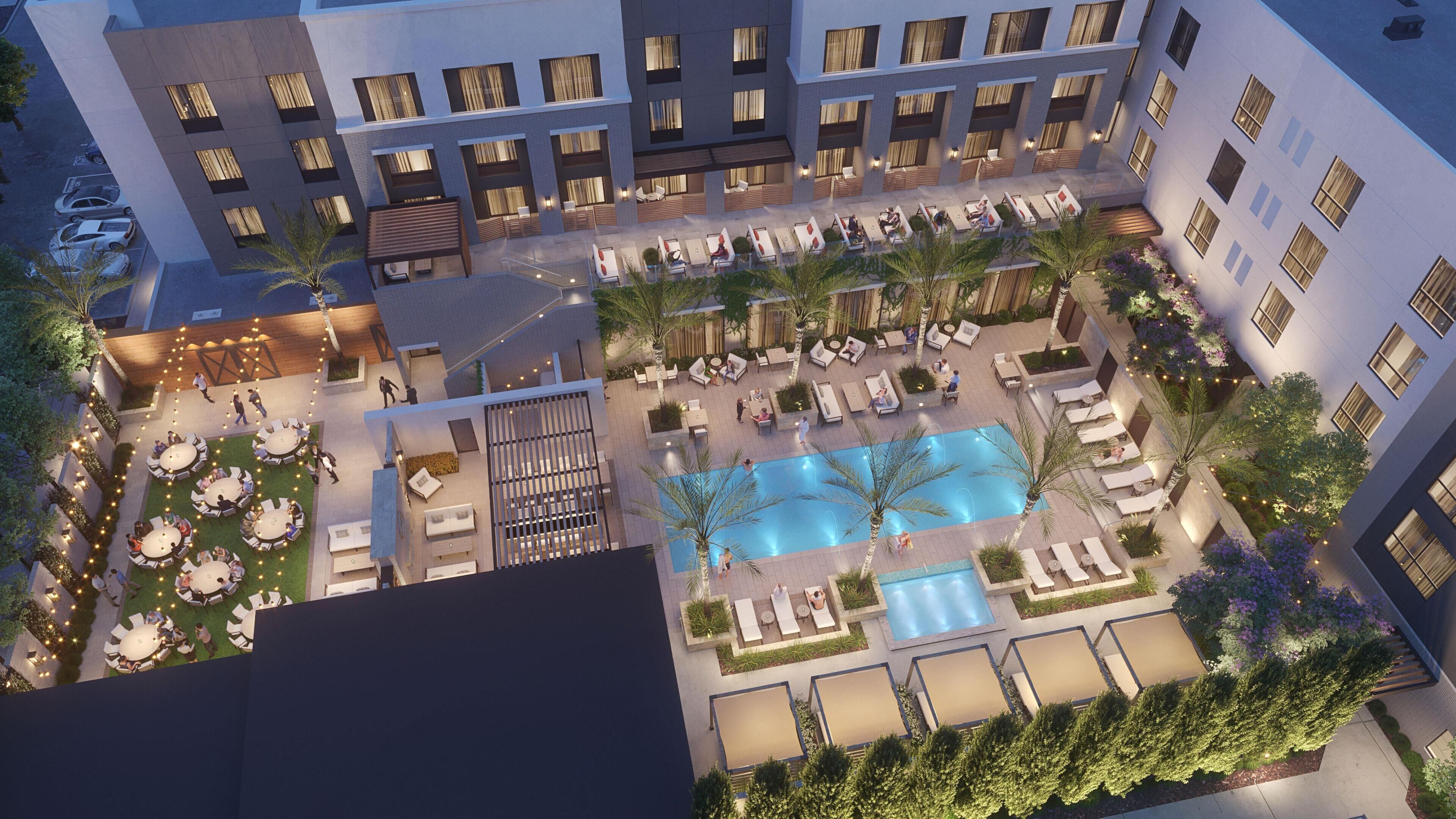 A hotel courtyard with a swimming pool, outdoor seating, and a covered area.