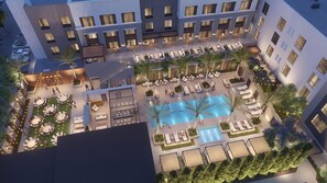 Un área de piscina en la azotea con sillas de descanso y mesas, rodeada por un edificio con múltiples ventanas.