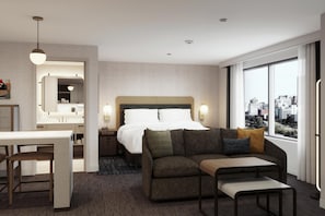 Una habitación de hotel con cama, sofá, mesa de comedor y un ventanal con vista a la ciudad.
