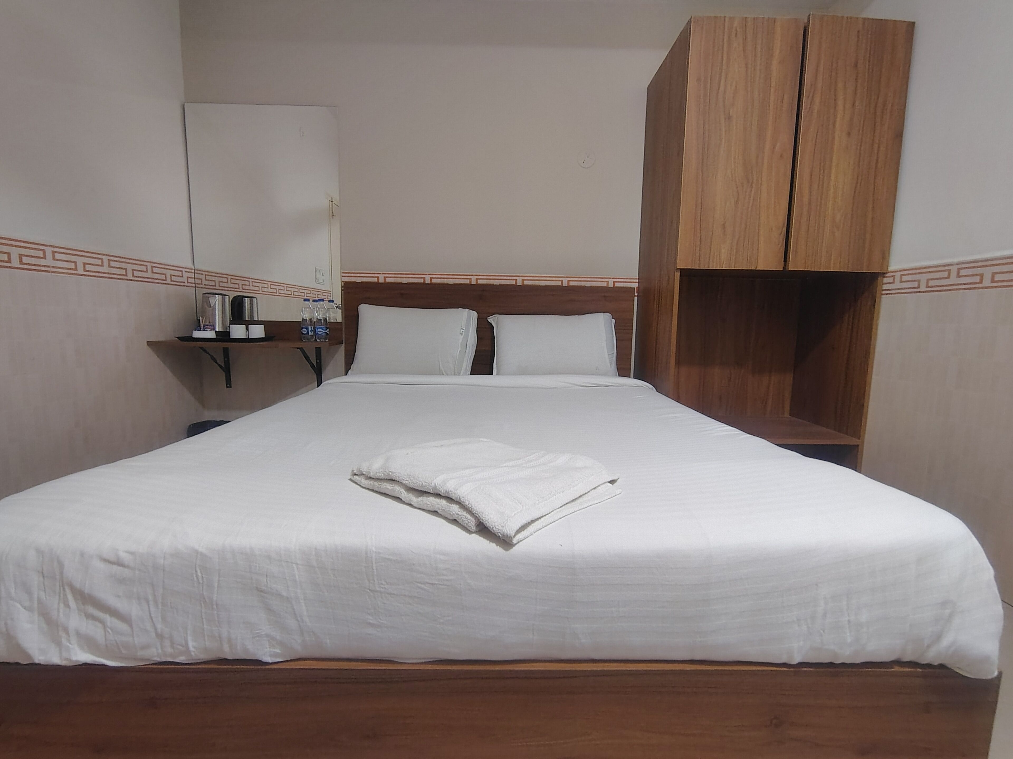 Habitación de hotel con una cama, un armario de madera, una mesita de noche con lámpara y un espejo instalado en la pared.