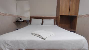 Habitación de hotel con una cama, un armario de madera, una mesita de noche con lámpara y un espejo instalado en la pared.