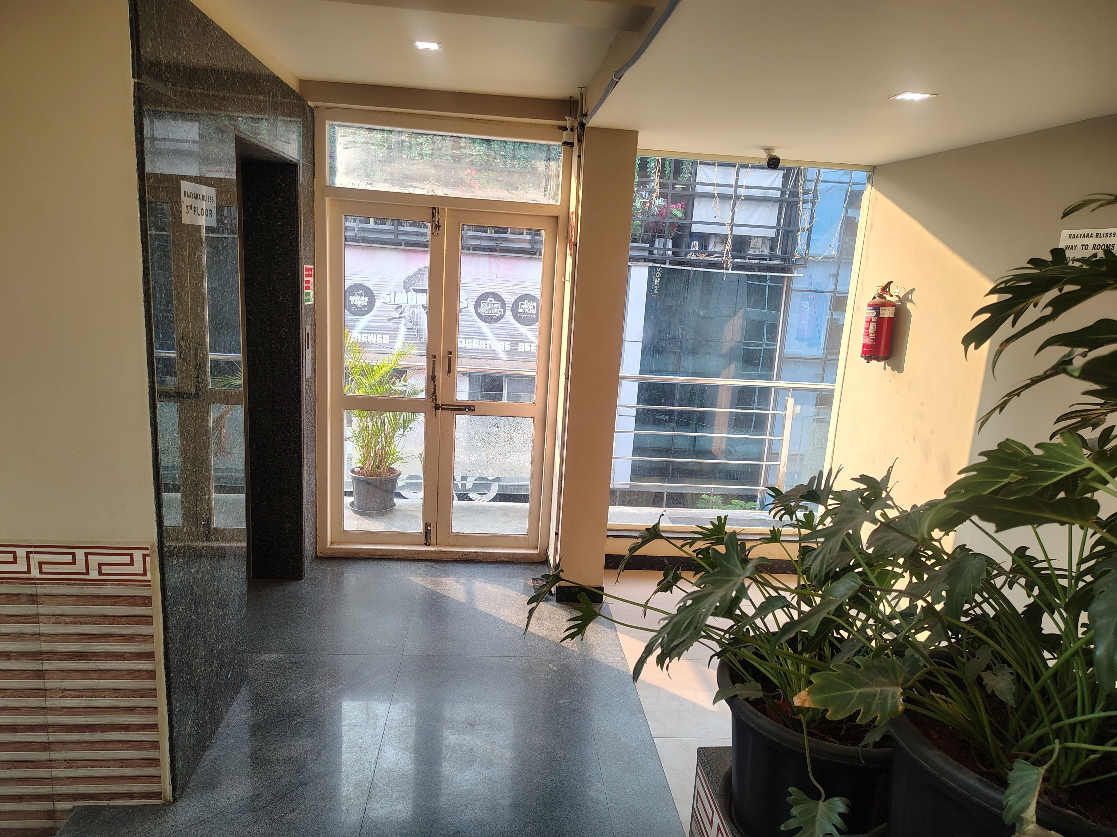 A hotel entrance with a glass door, a fire extinguisher on the wall, and potted plants.