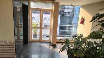 A hotel entrance with a glass door, a fire extinguisher on the wall, and potted plants.