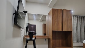 Ein Zimmer mit Schreibtisch, Stuhl, Kleiderschrank und einem an der Wand befestigten Fernseher.