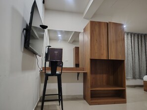 Een kamer met een bureau, een stoel, een kledingkast en een aan de muur bevestigde televisie.