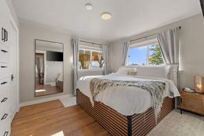 Ein Schlafzimmer mit einem großen Bett, einem Spiegel, einem Fernseher und einem Fenster mit Vorhängen.