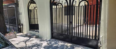 A gated entrance with a metal gate, a concrete pathway, and a car parked nearby.