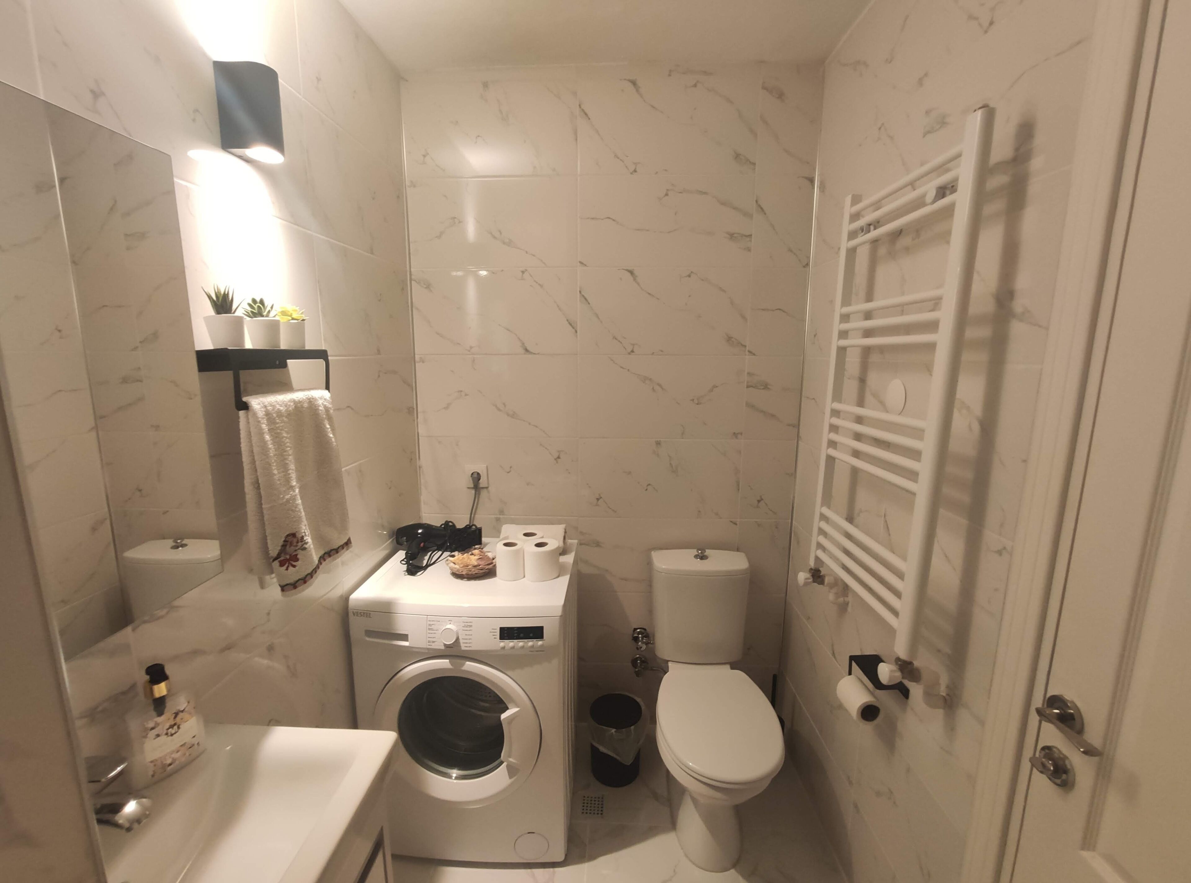 A compact bathroom with a washing machine, toilet, and a towel rack.