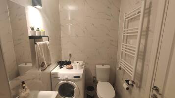 A compact bathroom with a washing machine, toilet, and a towel rack.